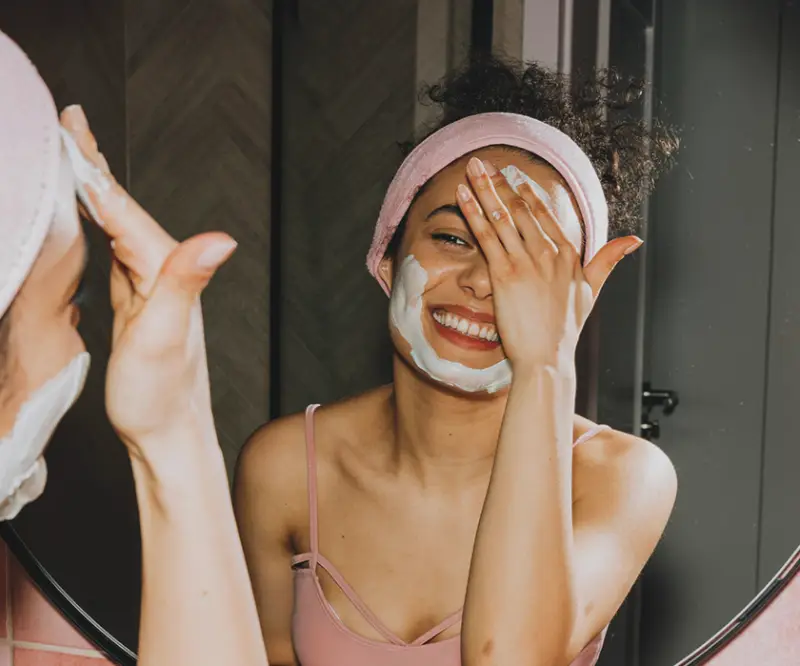 Mujer sonriente aplicando mascarilla facial, cuidado de la piel.